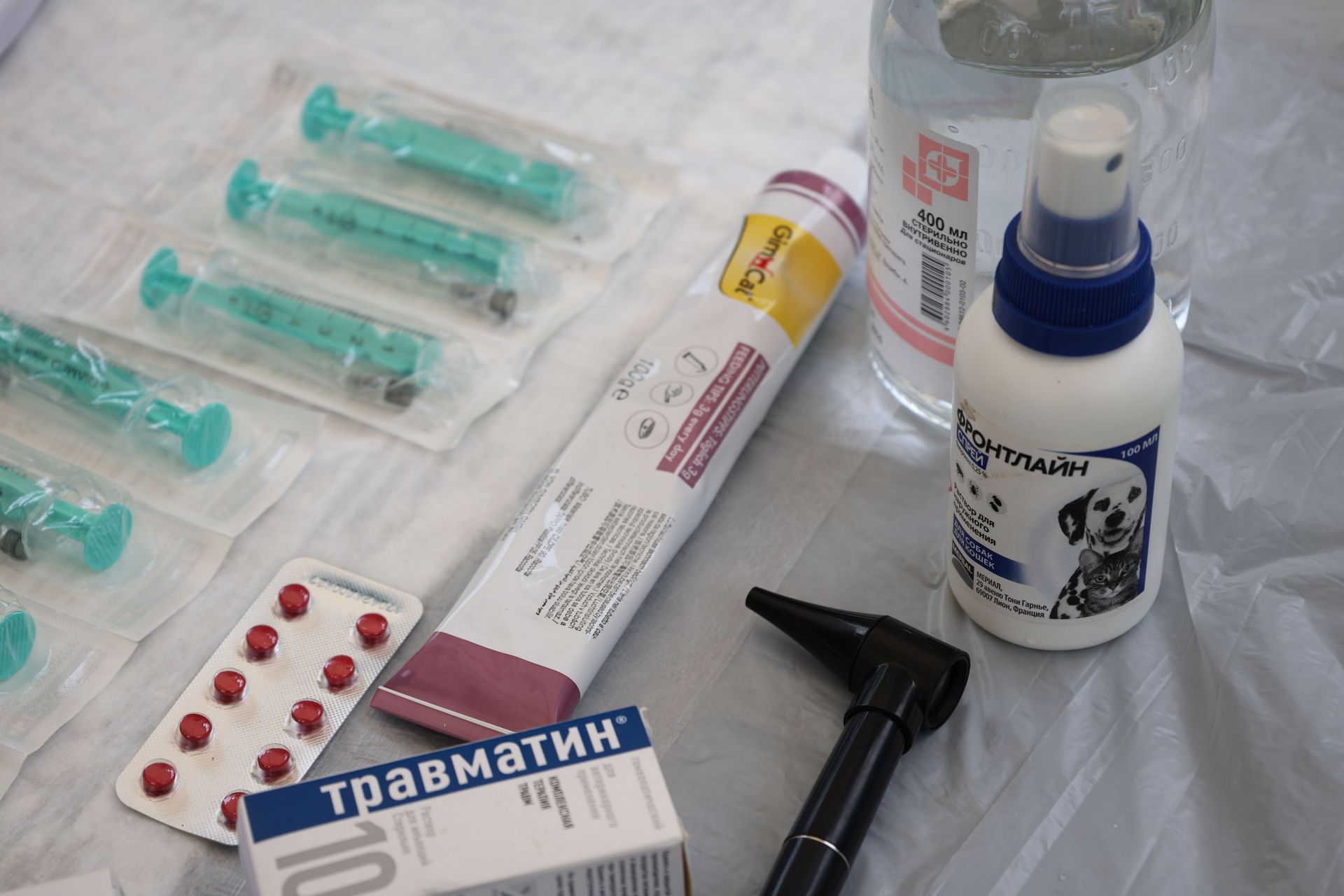 Medical supplies on a white table: syringes, pill packs, ointment, bottle, and a small hammer-like tool.