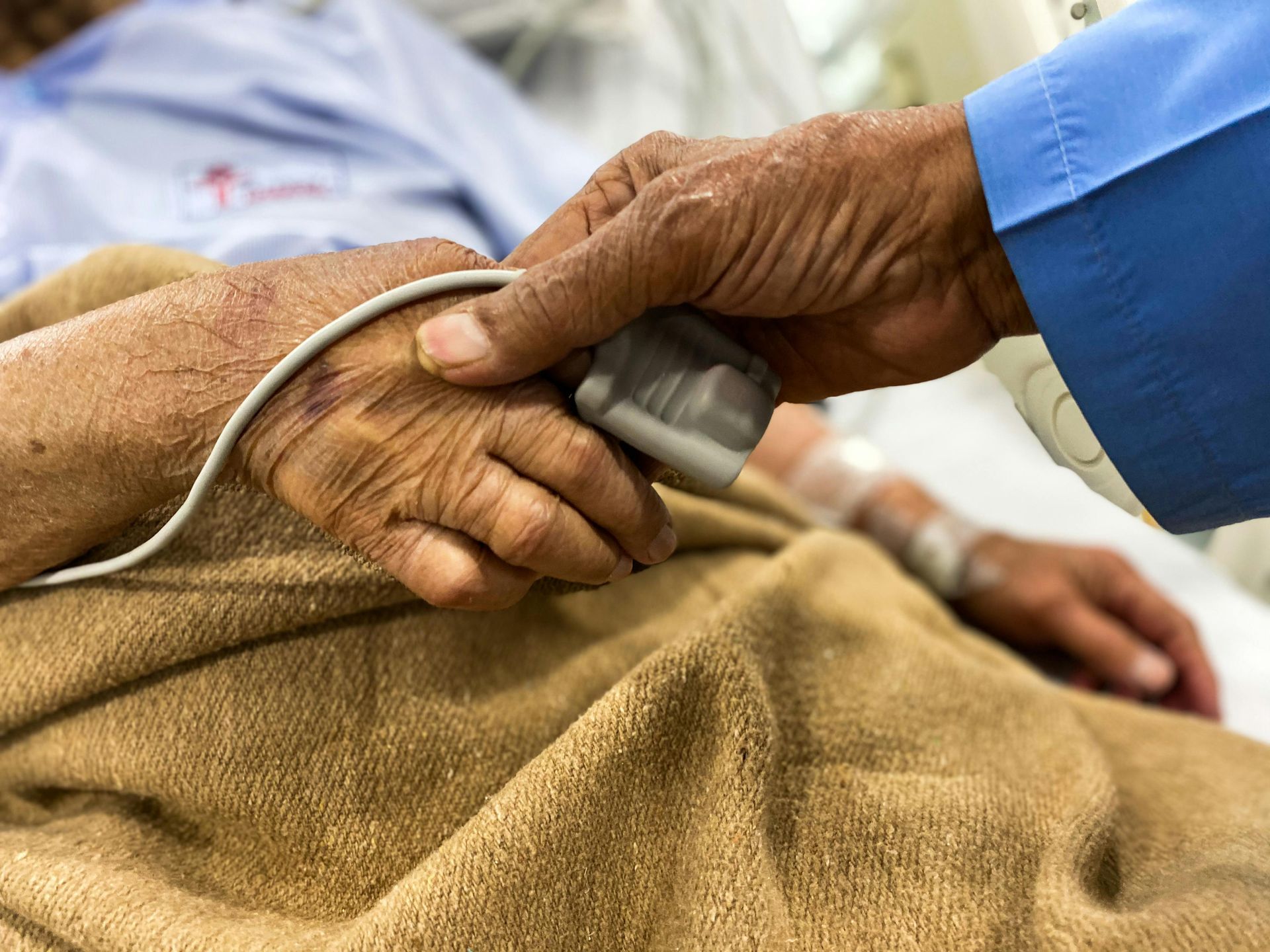 Hand holding an elderly patient’s hand with a blood pressure cuff in a hospital bed
