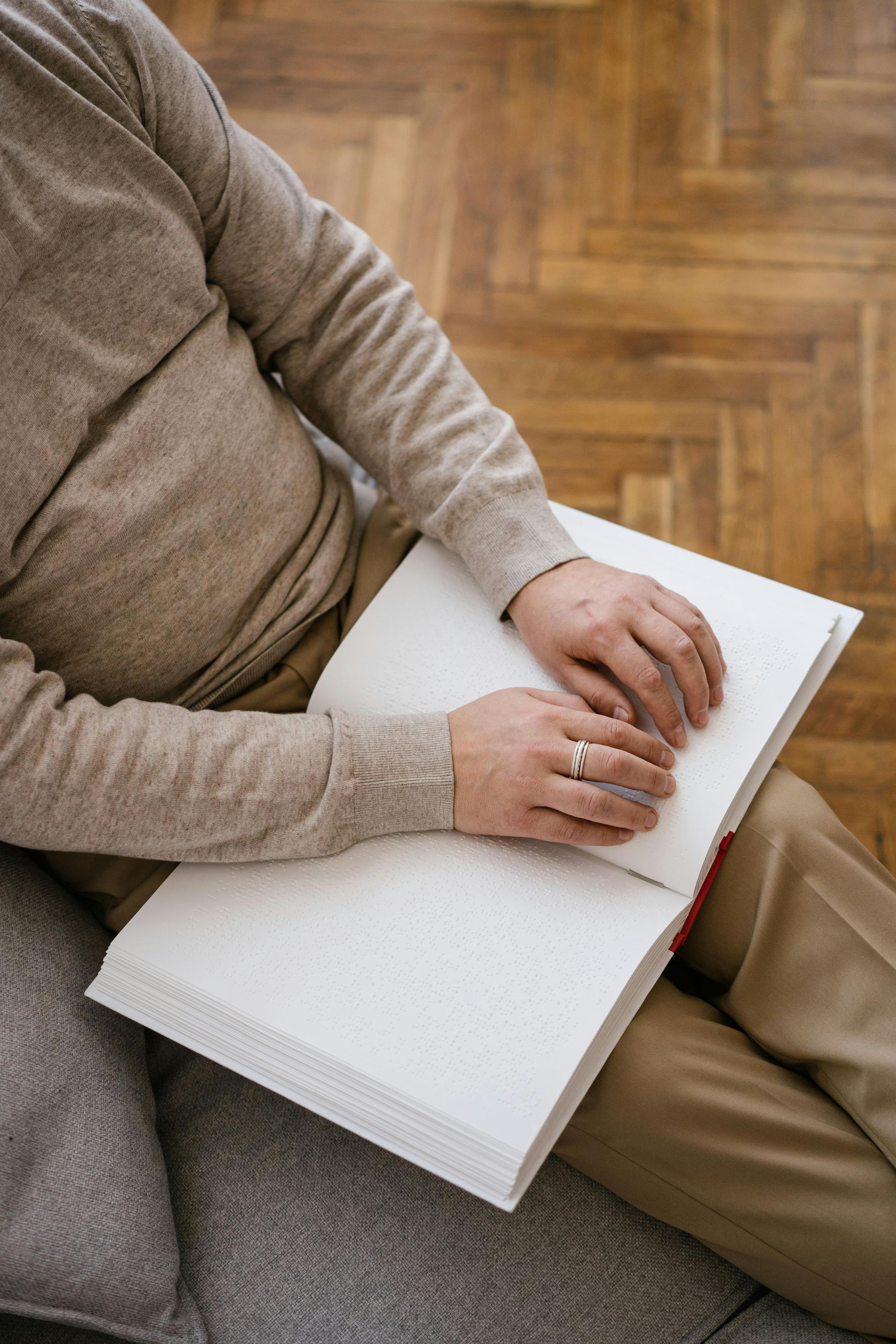 Person in a beige sweater writing in a white notebook on their lap while seated on a couch.