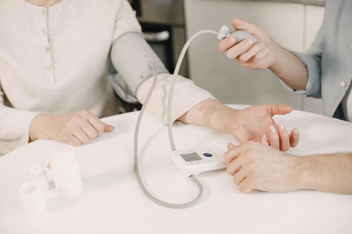 Person using a blood pressure monitor on another person’s arm at a white table