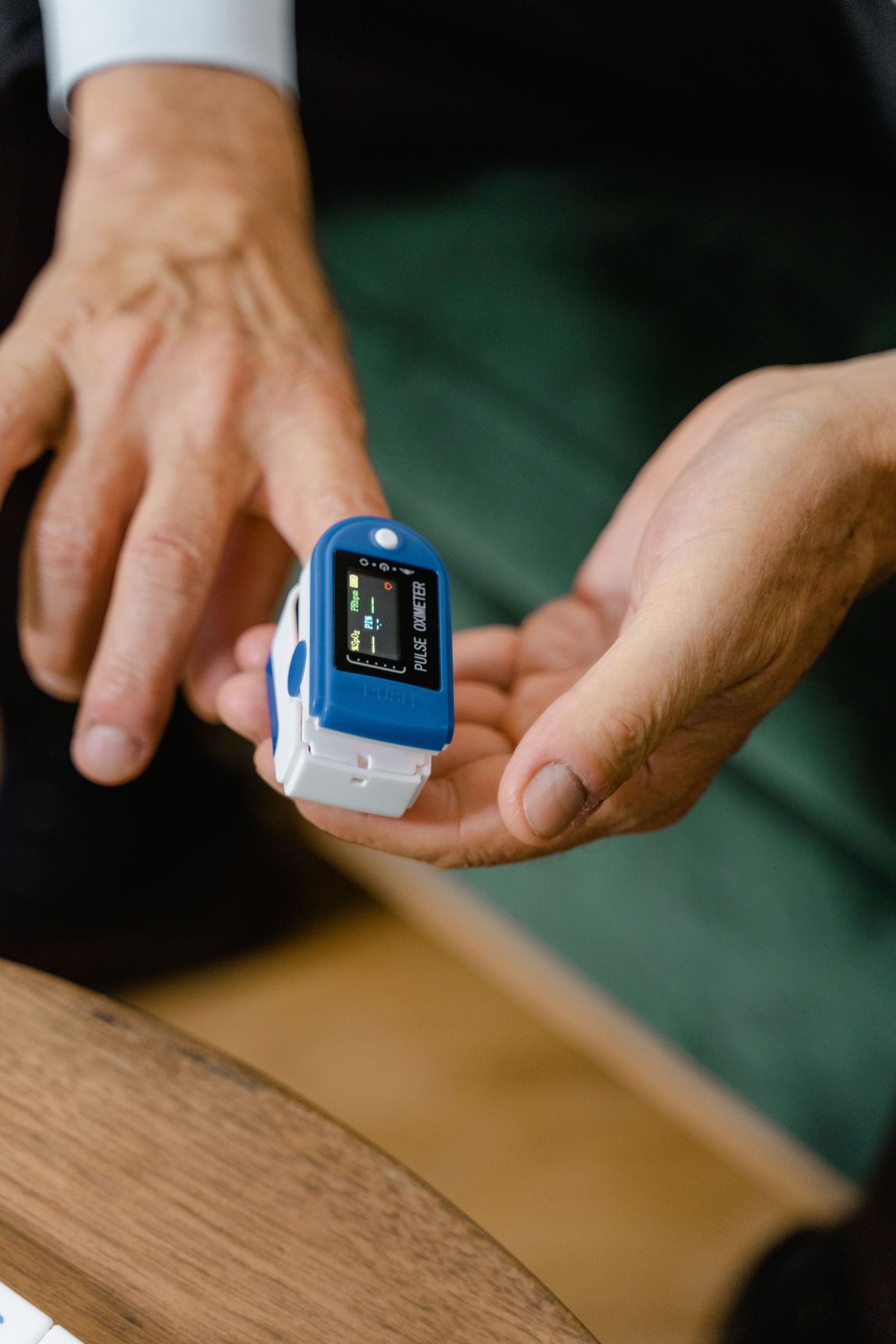 Hands holding a blue fingertip pulse oximeter with a lit display.