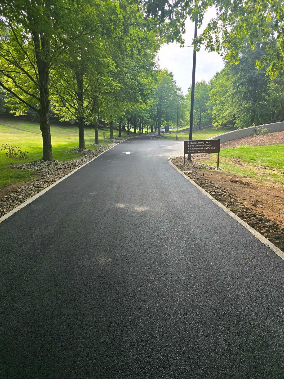 A road with trees on both sides and a bench on the side.