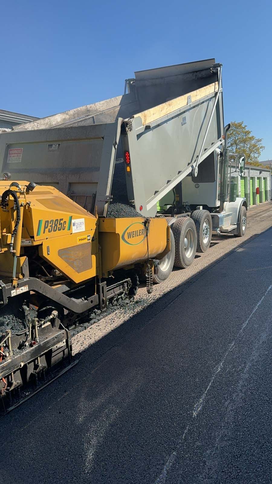 A dump truck is being loaded with asphalt on a road.