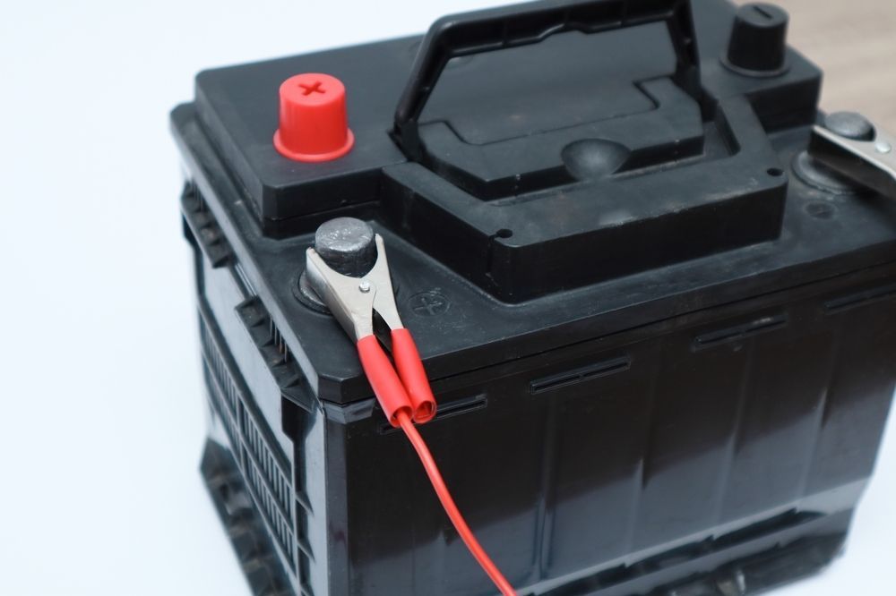 Black car battery with red and black clamps attached on a white background