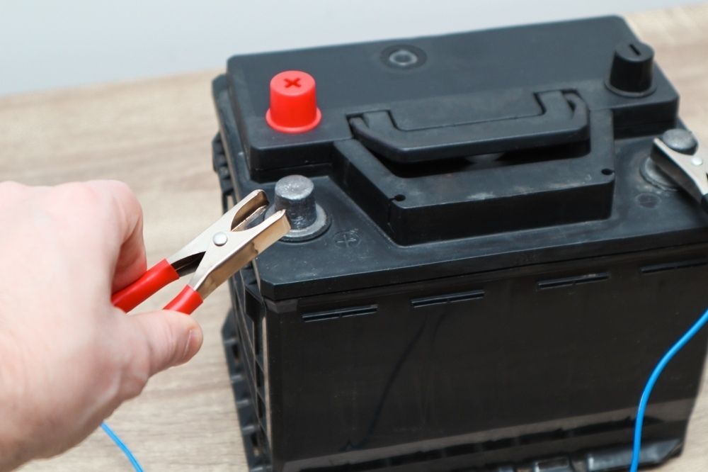 A Person is Charging a Car Battery With a Pair of Pliers — Central Coast Batteries In Tuggerah Lake, NSW