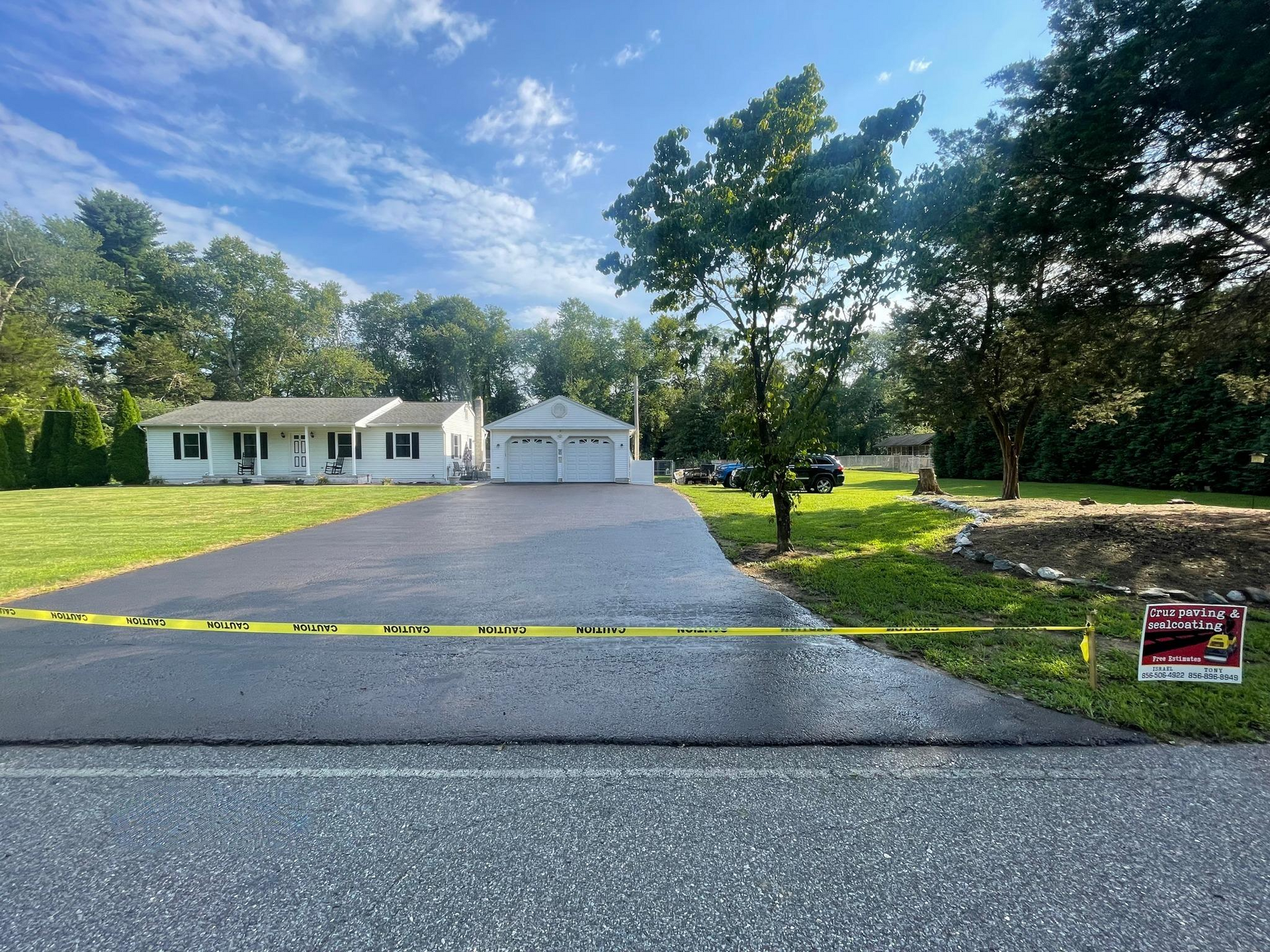 Single-story house with a long, new paved driveway, detached garage, and business sign for Cruz Paving & Sealcoating