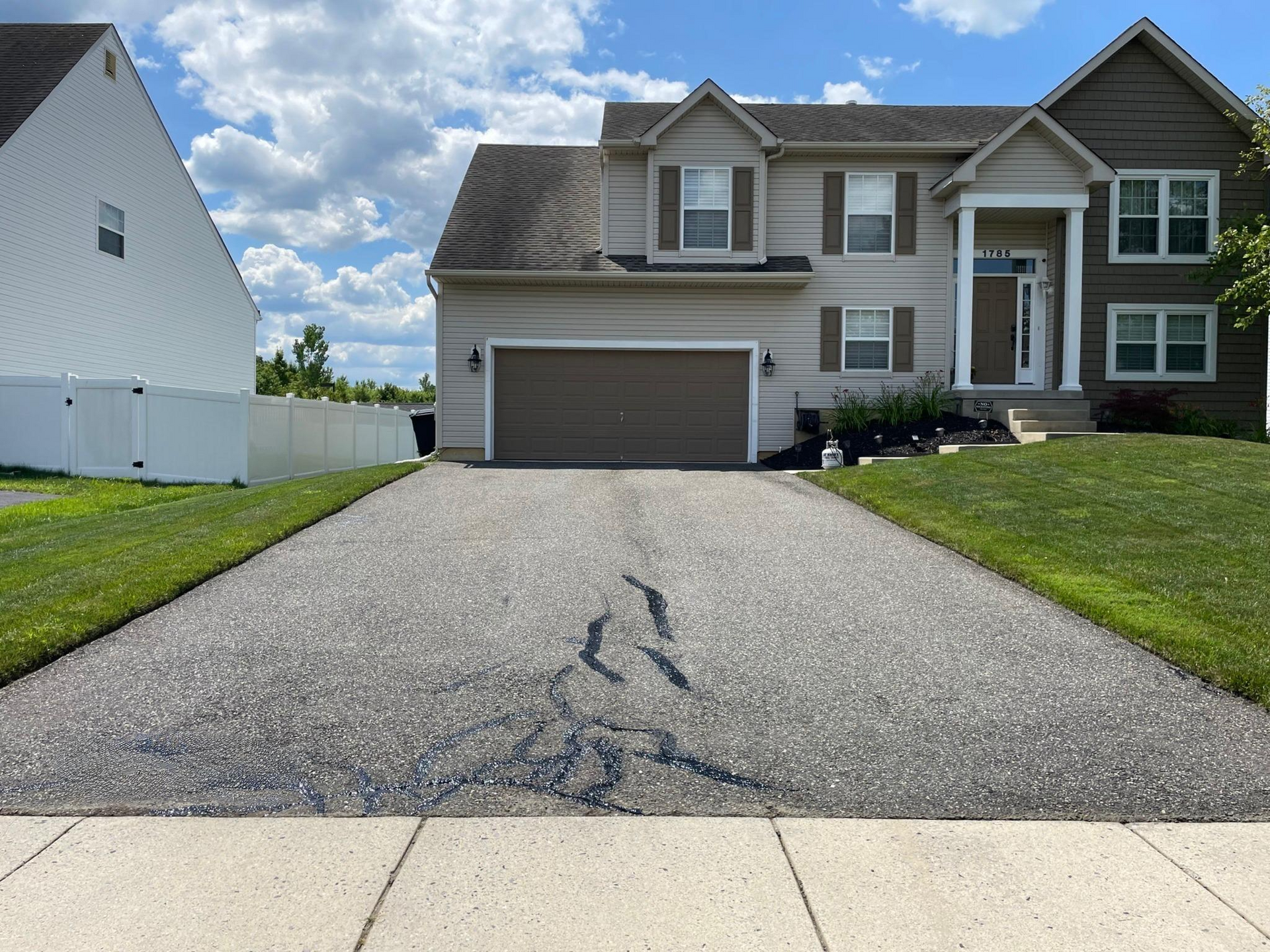 Suburban house with two-car garage and long cracked driveway under a cloudy sky