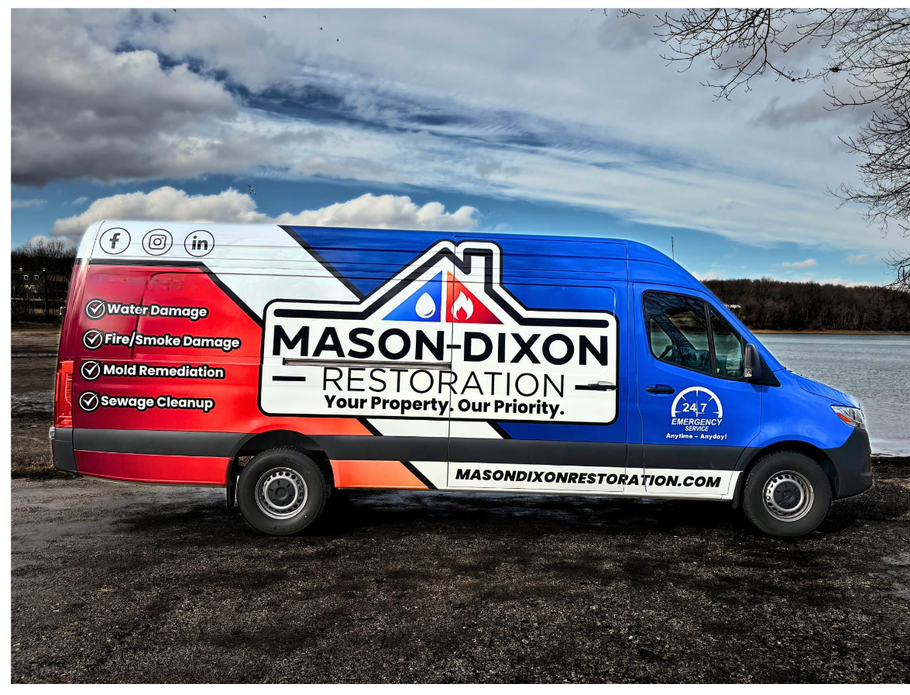 A red , white and blue van is parked next to a body of water.