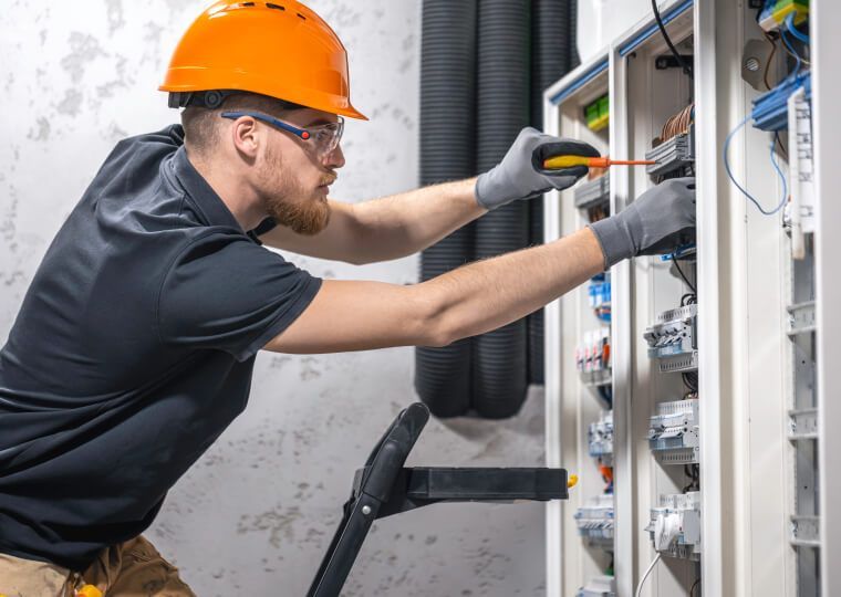 Electrician in orange hard hat wiring an electrical panel inside a utility room