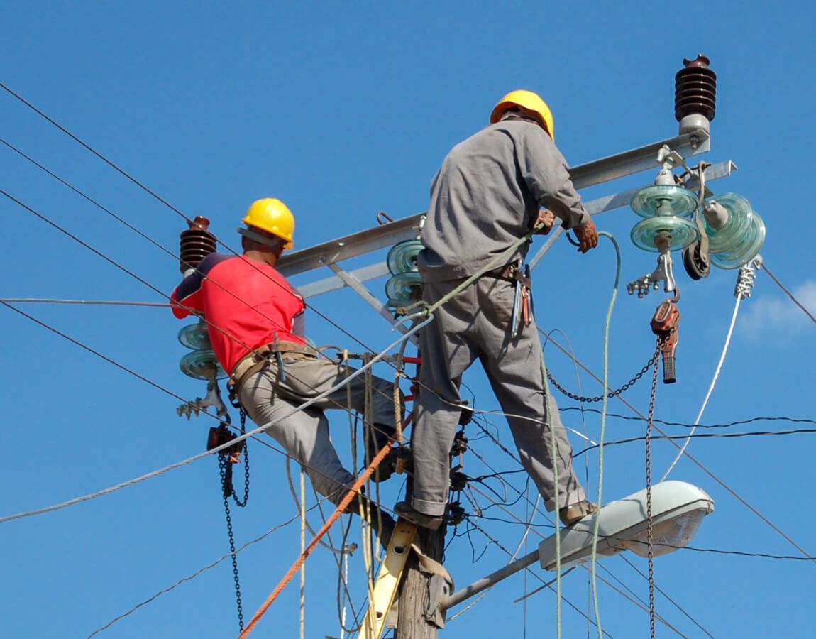 Utility workers on power lines with yellow helmets, repairing equipment against a blue sky