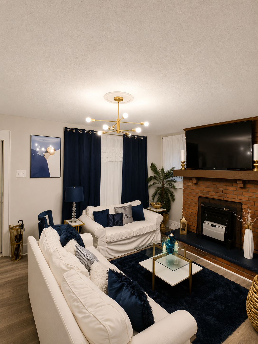 Cozy living room with white sofas, navy accents, fireplace, wall TV, and glass coffee table