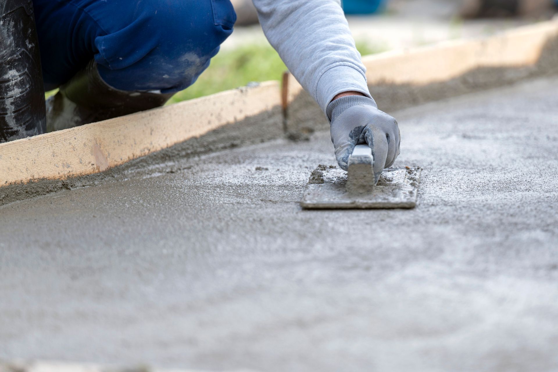 Worker smoothing wet concrete on a curb with a trowel.