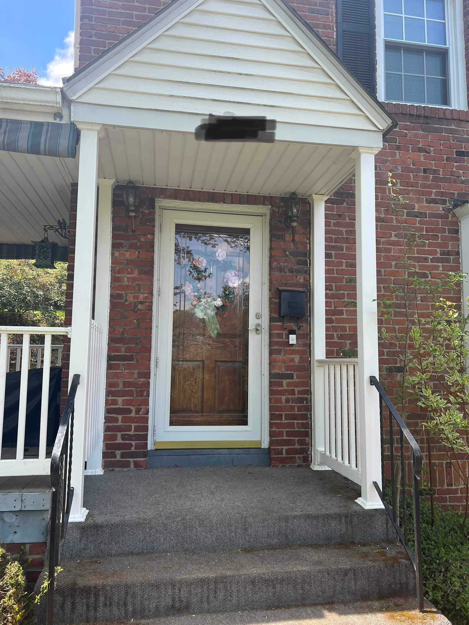 Brick house front porch with white railings and a wooden glass-paneled front door
