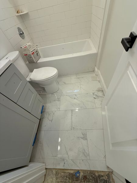 Small bathroom with a toilet, bathtub, gray vanity, and marble-pattern tile floor.