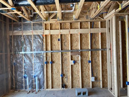 Exposed wall framing in an unfinished room with insulation, pipes, and a plastic-covered doorway