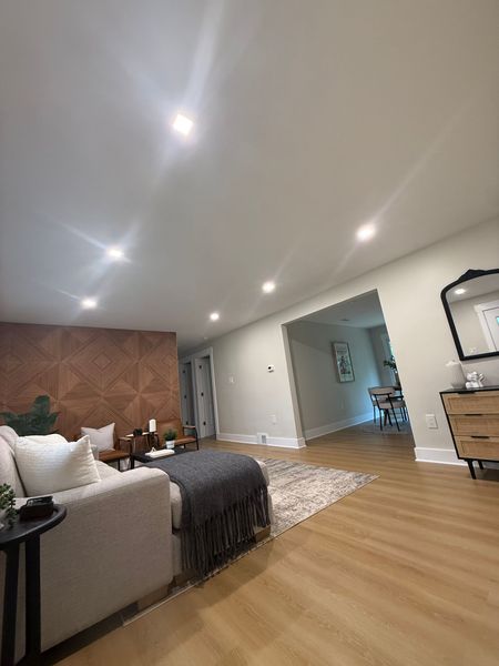 Bright modern bedroom with bed, wood accent wall, recessed lights, and open doorway to another room