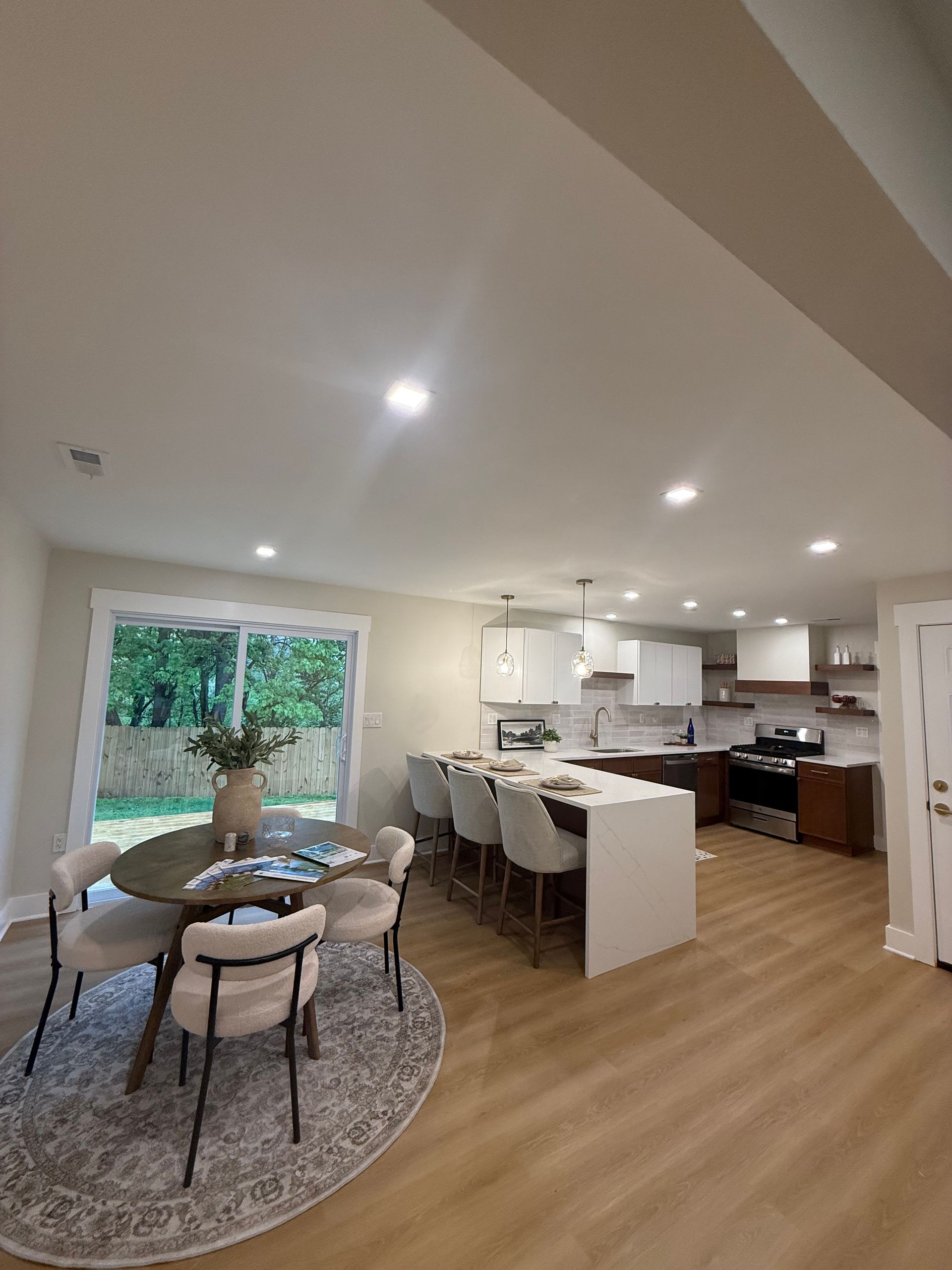 Bright open-plan kitchen and dining area with round table, island seating, and wood floors.