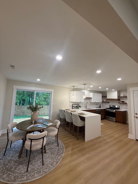 Open-plan kitchen featuring recessed lights and dining area with white island, dark cabinets, wood floors