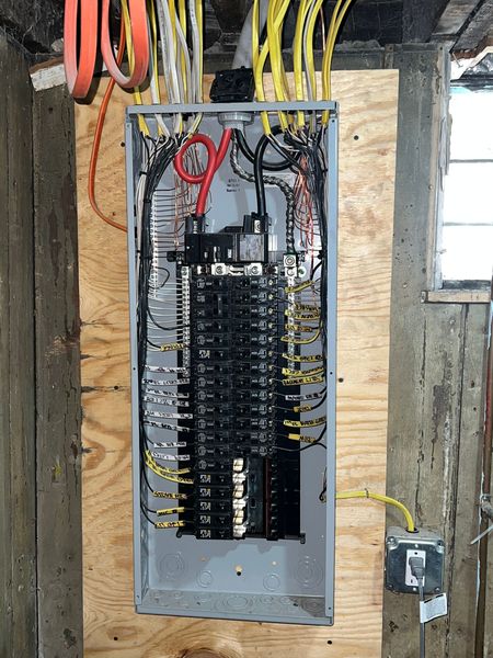 Open electrical breaker panel with exposed wiring in a workshop or unfinished room.