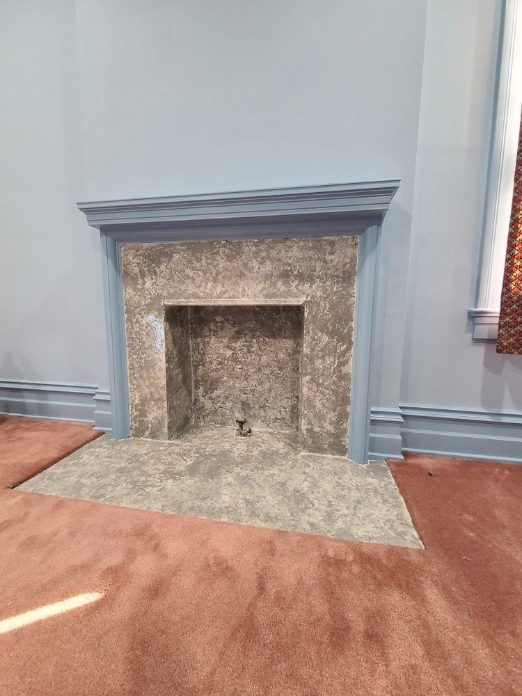 Empty fireplace with stone surround in a room with blue-gray walls and brown carpet
