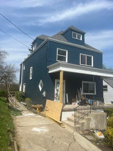 Blue two-story house with front porch and sloped driveway on a sunny day