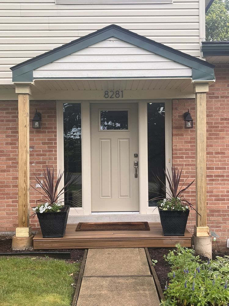 Front entrance of a brick house and timber posts with a beige door, small porch, and potted plants.