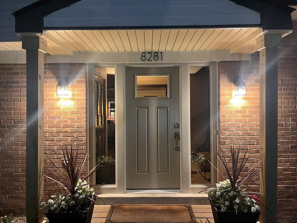 Front entrance of a brick house at dusk, with lit wall lamps and the number 8281 above the door.