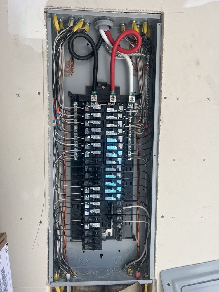 Open electrical breaker panel with exposed wiring and circuit breakers in a wall recess.