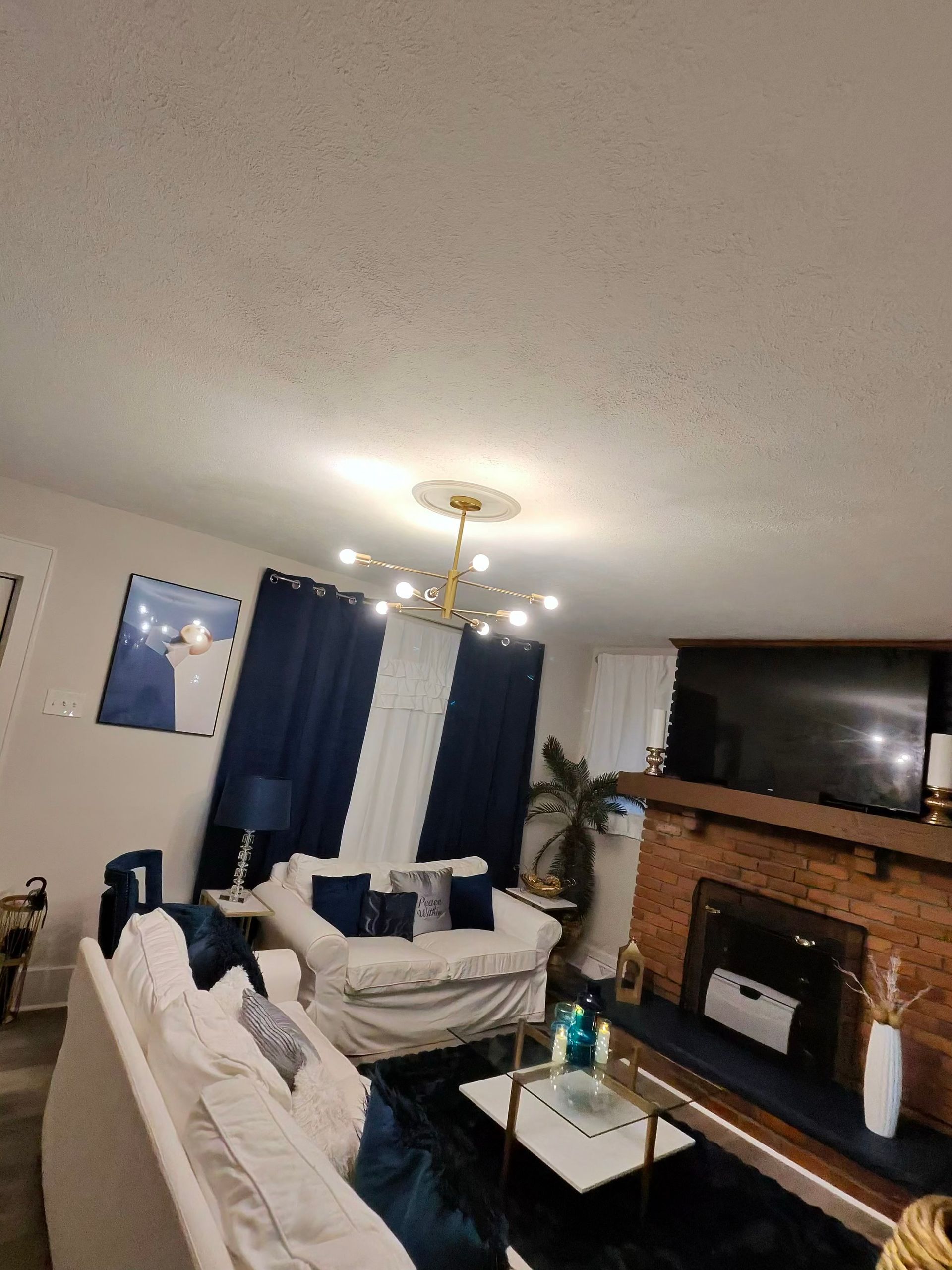 Living room with dark blue curtains, white furniture, a brick fireplace, and a chandelier.