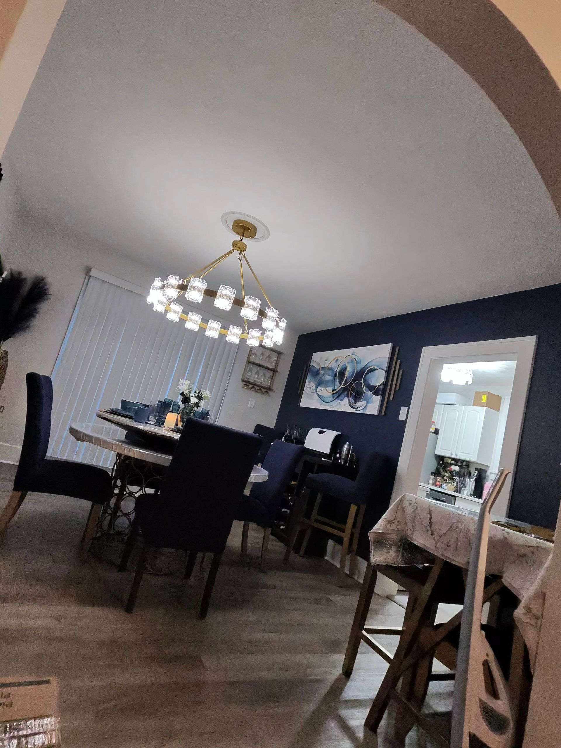 Dining room with dark chairs and table, chandelier, blue accent wall, and large wall art.