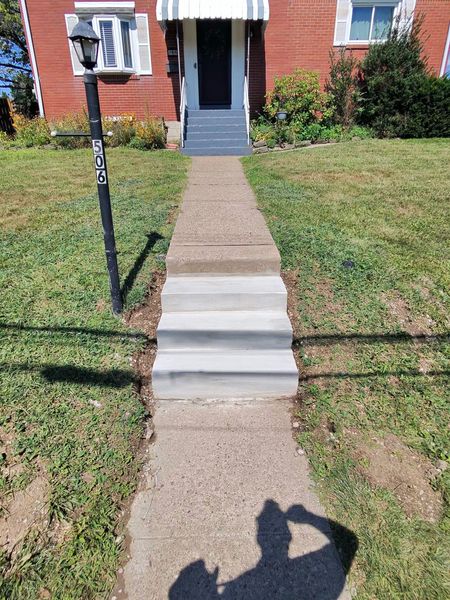 Front walkway with concrete steps leading to a brick house entrance, with a lamp post and grassy lawn.