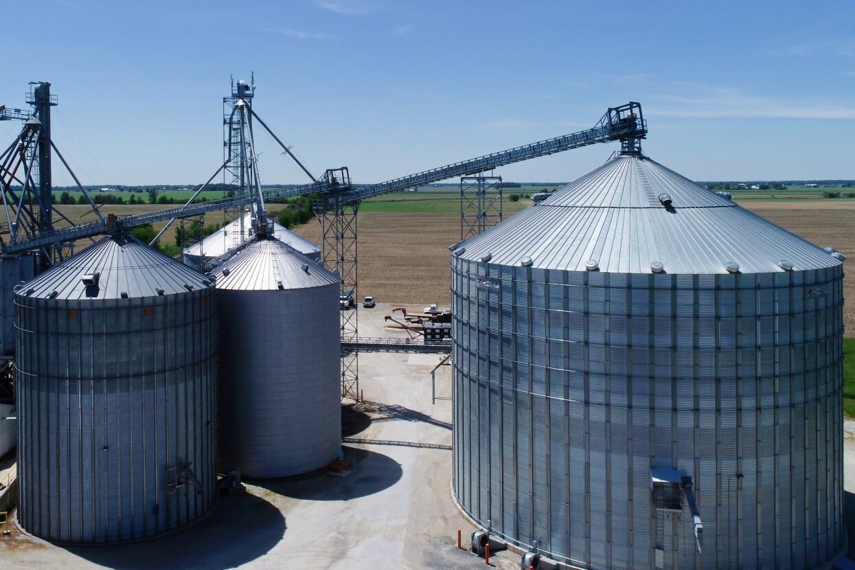 Aerial view of large metal grain silos and conveyor system in a rural farmyard