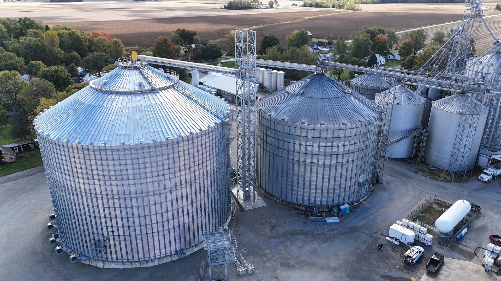Aerial view of large metal grain silos and storage tanks in an industrial agricultural yard.