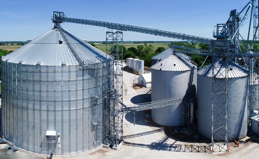 Large silver grain silos with conveyors at an industrial storage facility