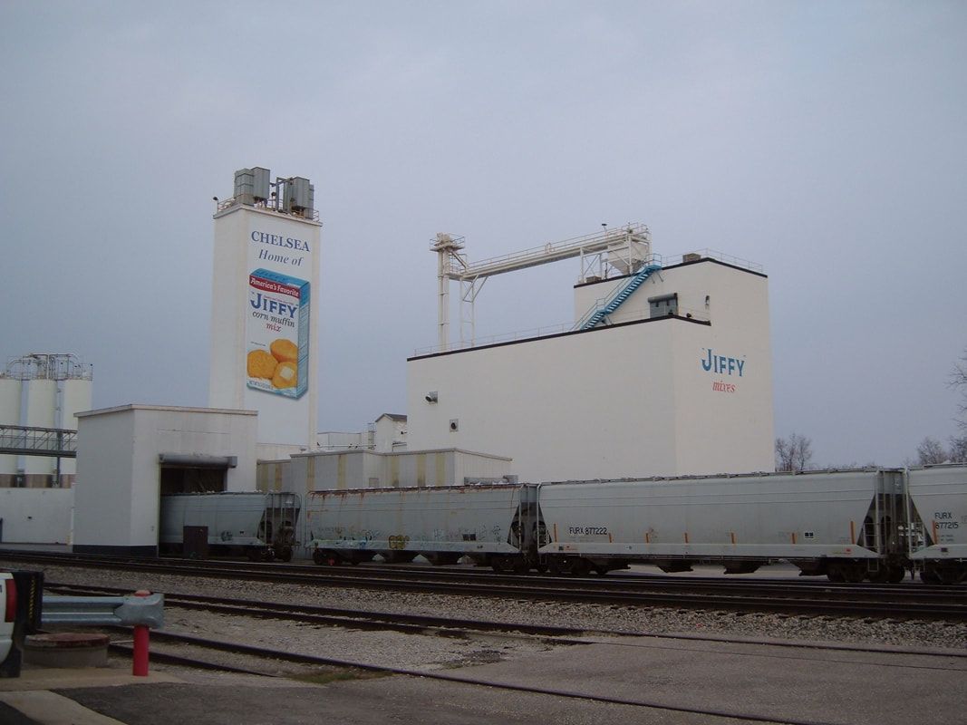 Industrial grain facility with white silos and rail cars under an overcast sky