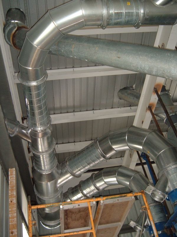 Silver HVAC ductwork and pipes running through an industrial ceiling above orange scaffolding.