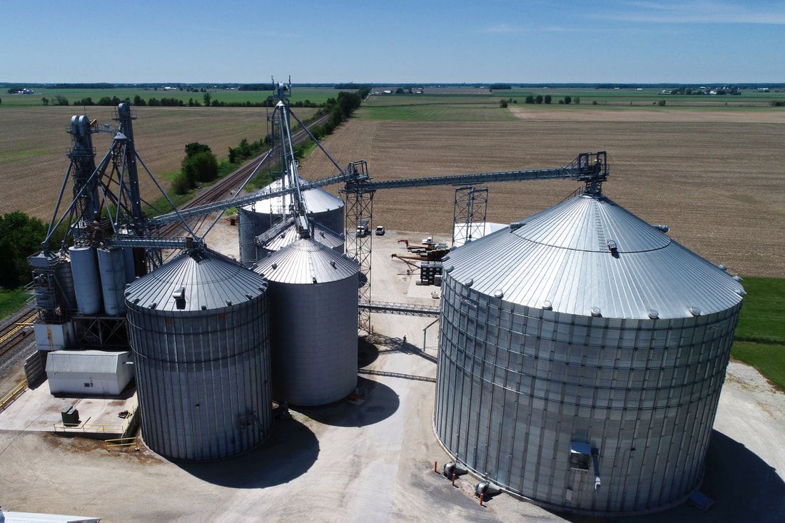 Aerial view of three metal grain silos and conveyors in a rural farm field
