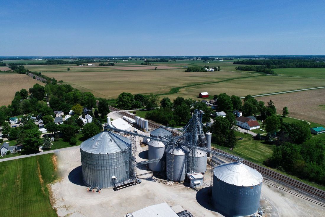 Aerial view of a farm with silver grain silos and bins beside fields and rural buildings