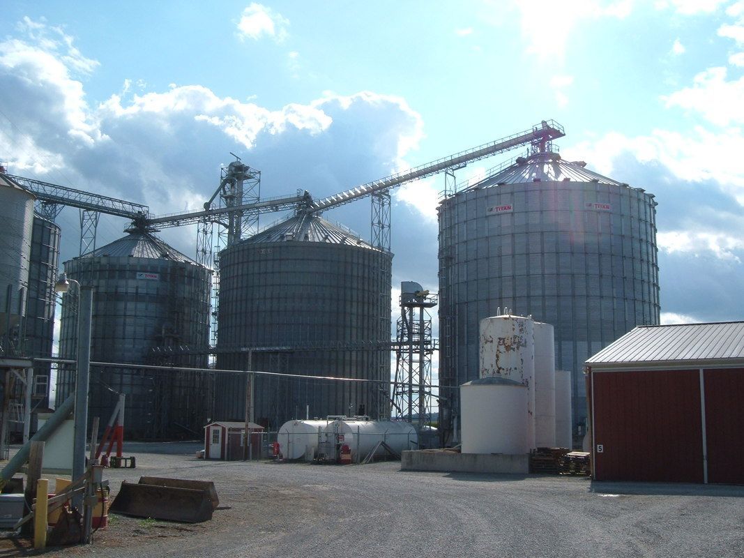 Large grain silos and conveyors at an industrial site under a partly cloudy sky