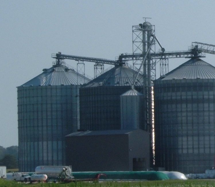 Grain silos and storage tanks at an industrial facility under a cloudy sky
