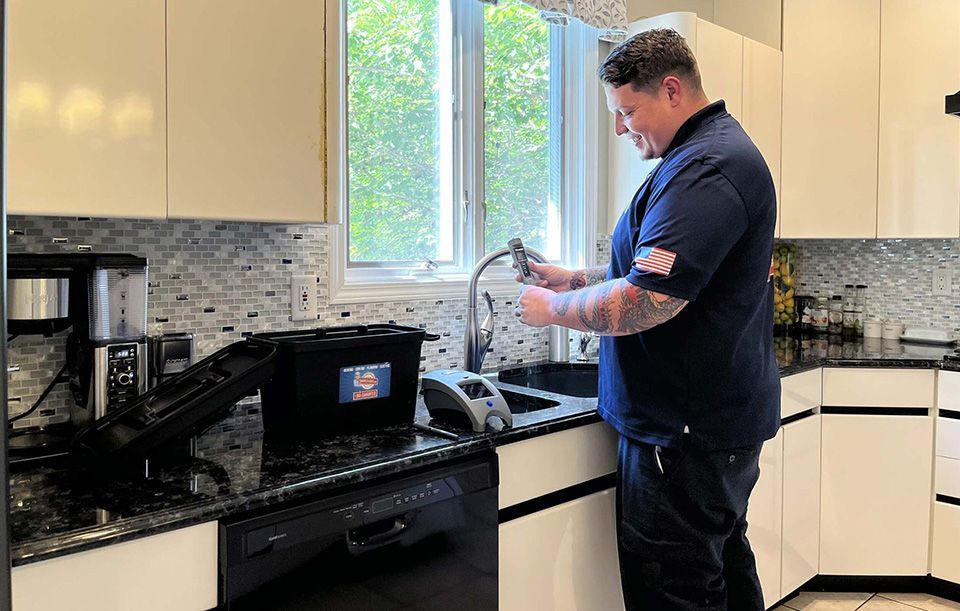 Man washing dishes at a kitchen sink beside a black stove and countertop coffee maker.