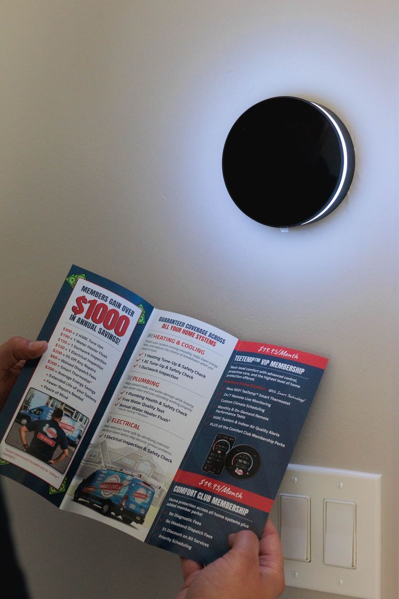Hand holding an open brochure beside a round wall light and a white light switch panel