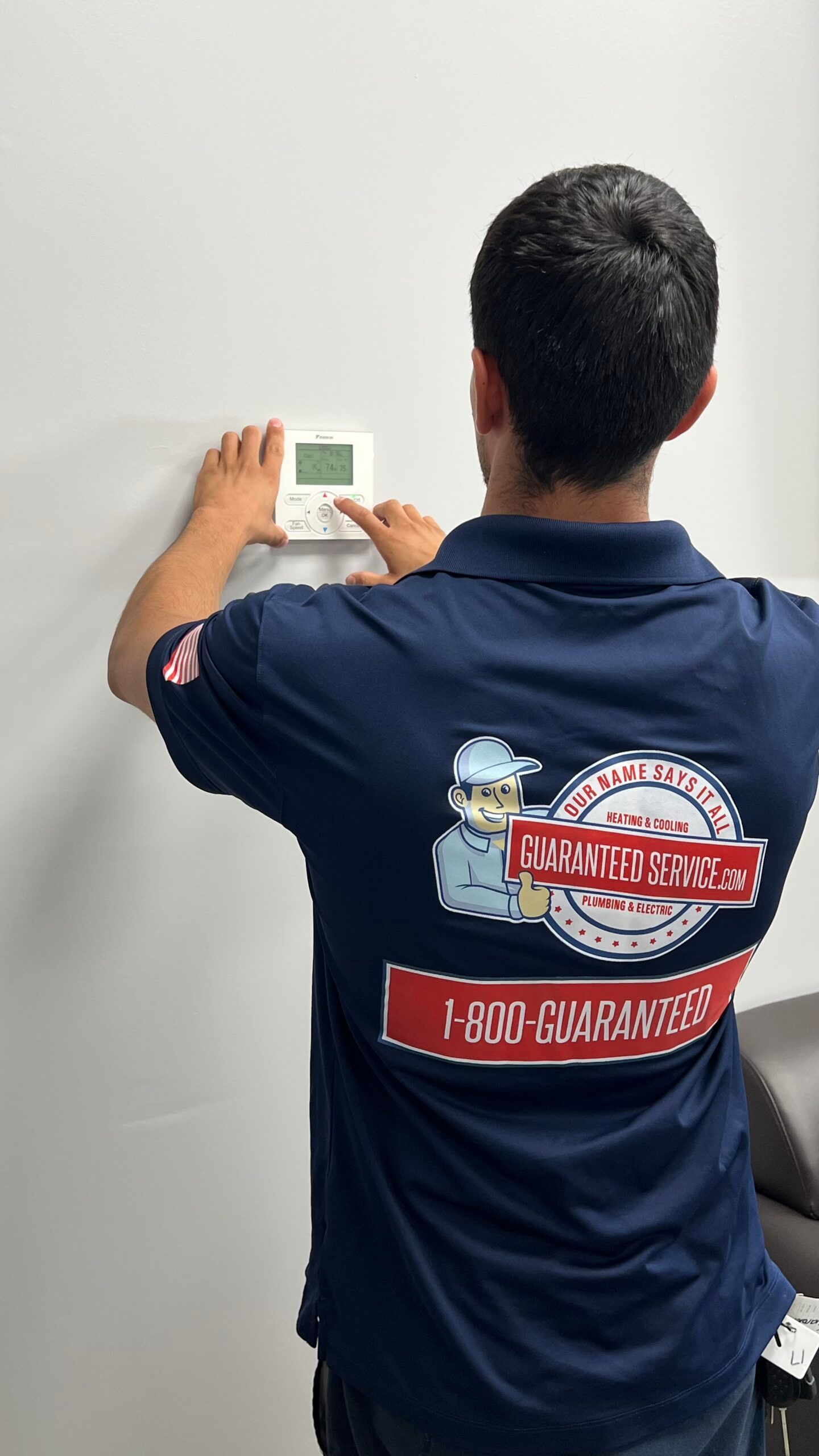 A man in a blue shirt is adjusting a thermostat on a wall.