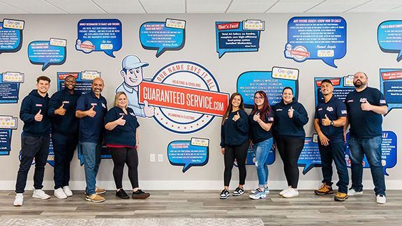 Group of employees posing before a wall mural, holding a banner that says “Customer Service.”