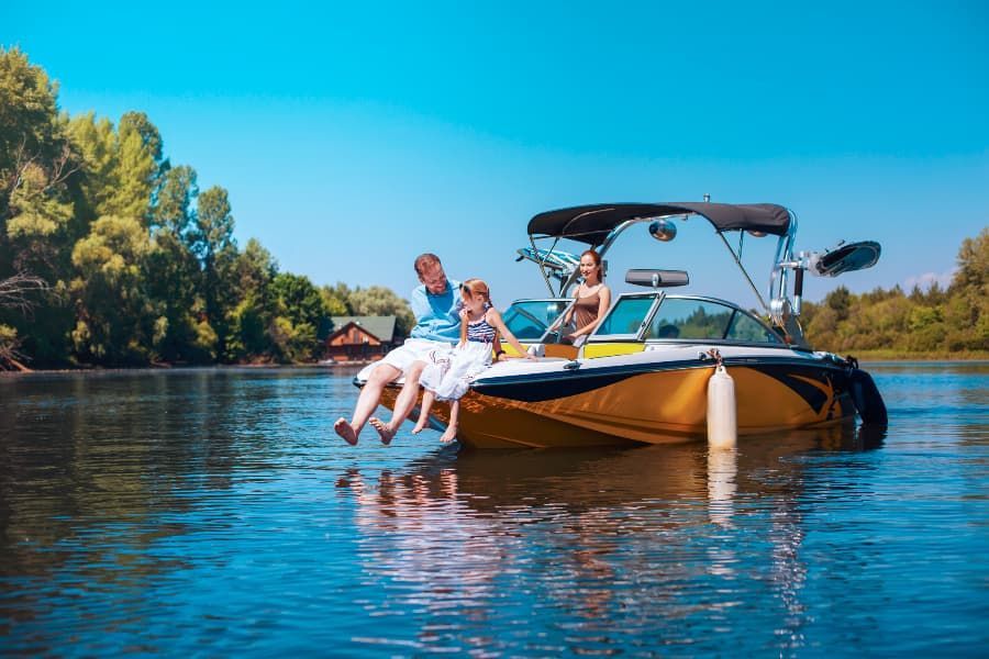 A family on a boat with a man and his daughter dangling their feet over the side. 