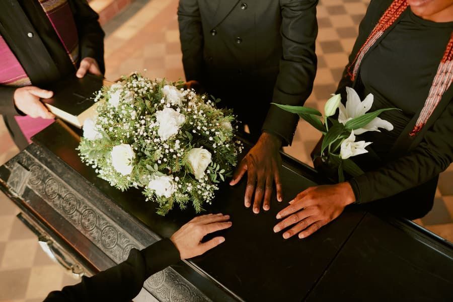 Close-up of people putting their hands on a coffin at a funeral. 