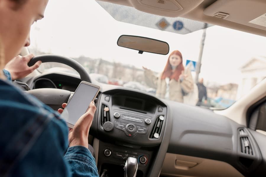 Wrecked bicycle, helmet, and eyeglasses on road in front of white car Distracted male driver looking at phone about to hit female pedestrian