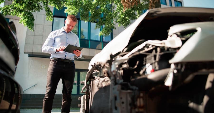 Insurance adjuster looking down at a tablet while inspecting a vehicle after a car accident. 