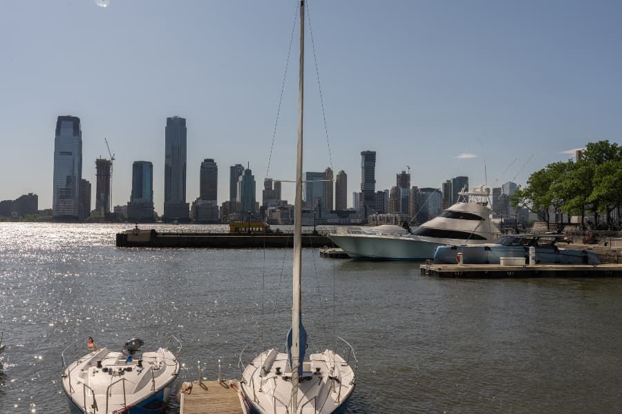 Wrecked bicycle, helmet, and eyeglasses on road in front of white car Boats in harbor with New York skyline in background.
