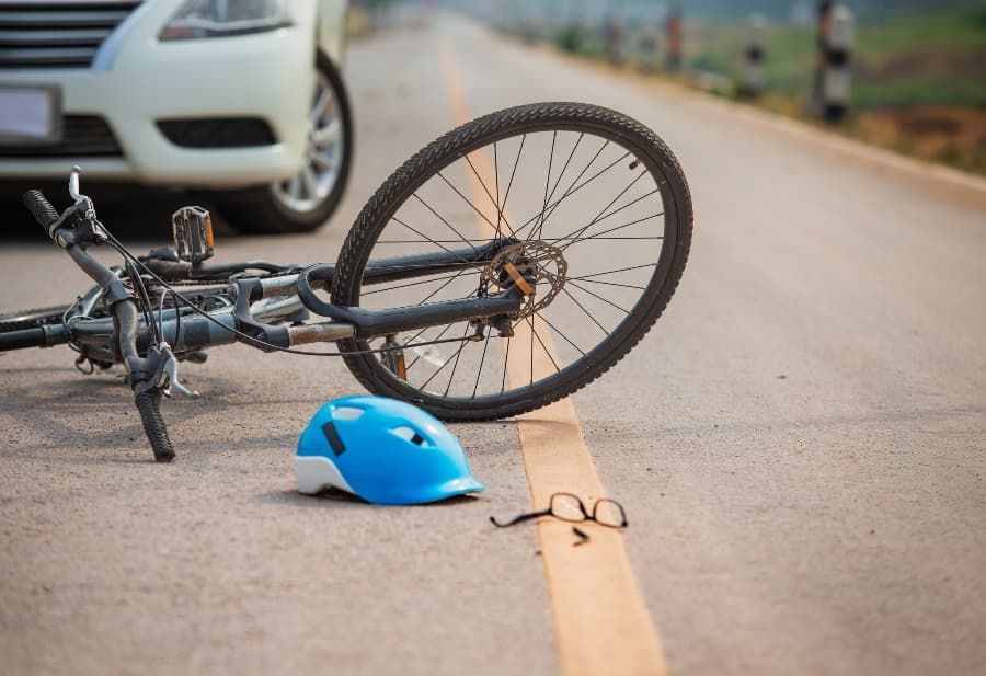 Wrecked bicycle, helmet, and eyeglasses on road in front of white car 